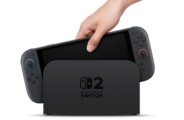 A hand reaching down to pull a Nintendo Switch 2 out of its dock