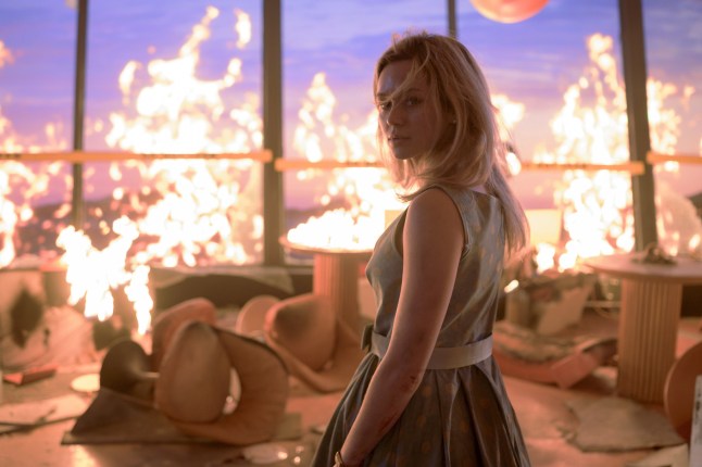 Brec Bassinger as Iris Campbell in Final Destination: Bloodlines. She is standing in a restaurant with large glass windows surrounded by flames